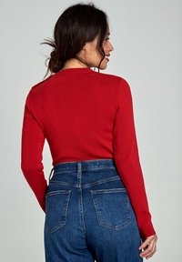 Czerwona, prążkowana sweter z długim rękawem, dopasowany krój i wysoki dekolt, w połączeniu z niebieskimi dżinsami z wysokim stanem z tylnymi kieszeniami.