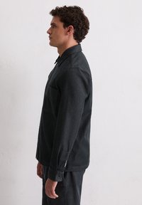 Czarna koszula z denimu z kołnierzykiem, z kieszenią na piersi, zapinana na guziki mankiety oraz luźnym krojem. Miękka faktura i jednolity kolor z minimalnymi detalami.