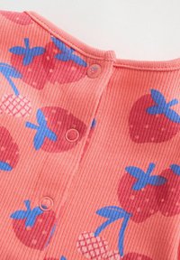 Tissu côtelé corail avec imprimés de fraises bleues et rouges, boutons-pression corail assortis, montrant une partie de l'encolure d'un vêtement.