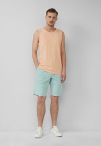 Débardeur pêche clair avec un col rond, associé à un short vert menthe. Des baskets blanches complètent l'ensemble, sur un fond neutre.