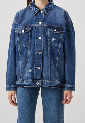 Chaqueta de mezclilla en azul medio con herrajes plateados, cierre frontal con botones, dos bolsillos en el pecho y acentos desgastados. Corte oversized con cuello clásico.