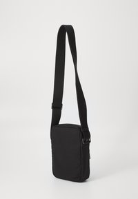 Borsa a tracolla nera realizzata in morbido tessuto, forma rettangolare, tracolla regolabile, chiusura con zip e design minimalista senza logo visibile.