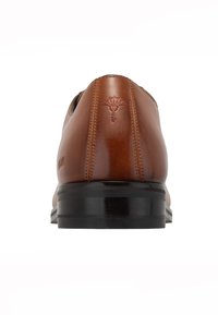 Brązowy skórzany elegancki but o gładkim wykończeniu, zaokrąglonym nosku i czarnej gumowej podeszwie. Posiada przeszycia dekoracyjne oraz tłoczone logo na pięcie.