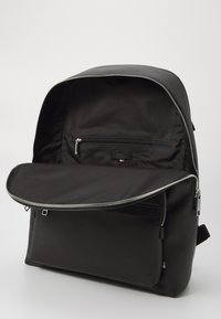 Sac à dos en tissu noir avec une ouverture zippée, texture lisse, poche intérieure et accessoires métalliques. Conçu pour la fonctionnalité et l'organisation.
