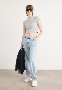 Sivi kratki top s kratkim rukavima, svijetloplava široka traperica s tie-dye akcentima, bijele tenisice i tamnoplava traper jakna. Crne sunčane naočale.