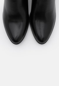 Czarne skórzane botki za kostkę z szpiczastym noskiem, o gładkim wykończeniu i eleganckim designie, z minimalistycznymi liniami i bez widocznych elementów metalowych.