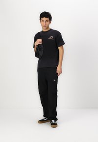 Black t-shirt with a small logo, paired with black cargo pants featuring side pockets and black sneakers with white laces and brown soles.