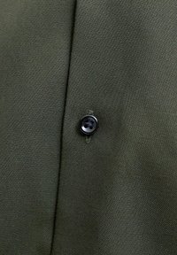 Κοντινή λήψη πράσινου υφάσματος με ραφή και μαύρο κουμπί με τέσσερις τρύπες, ραμμένο με ταιριαστή κλωστή.