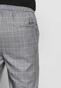 Grey plaid trousers with elastic waistband and a small back pocket, worn with a black top.