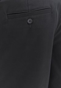 Gros plan sur un pantalon en tissu noir avec une poche fendue sécurisée par un bouton unique et une couture soignée au-dessus de la poche.