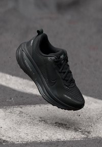 Crne Nike tenisice za trčanje s teksturiranim gornjim dijelom i glatkim potplatima, koje imaju zaobljeni vrh, vezice i suptilni brend.