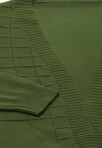 Zöld kötött pulóver bordázott V-nyakkal, texturált panellel és kontrasztos bordázott mandzsettákkal. Puha anyag, sima felülettel.