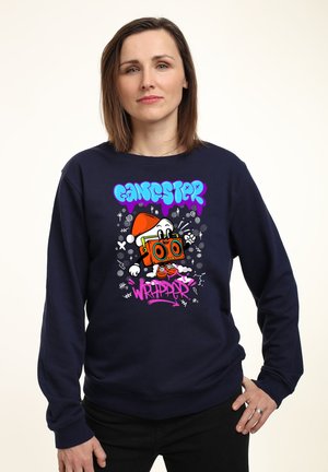 Felpa blu marina con design grafico che presenta un personaggio dei cartoni animati con una macchina fotografica, testo colorato e dettagli giocosi. Maniche lunghe con polsini a costine.
