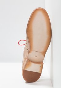 Semelle de chaussure en cuir tan avec des lacets rouges, dotée de perforations détaillées et d'une finition lisse. Taille 37 et gravure de marque visible.