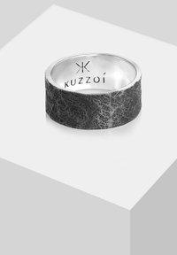 Anello a fascia nera texturizzata con interno in argento, caratterizzato da un bordo liscio e un logo "Kuzzôi" inciso all'interno. Design distintivo con contrasti audaci.