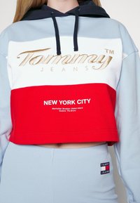 Korta sweatshirt i blått, vitt och rött. Utrustad med guldbroderad "Tommy"-logotyp och "NEW YORK CITY" tryckt i vitt. Tyget har en mjuk textur.
