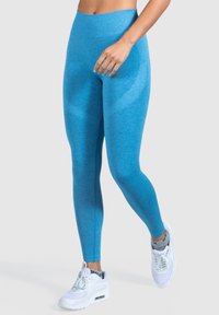 Leggings a vita alta, aderenti, in tessuto blu brillante, con una texture liscia e un design semplice. Abbinati a sneaker bianche.