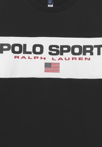 Svart bomull t-shirt med ett framträdande vitt horisontellt band med "POLO SPORT" och "RALPH LAUREN" i svart och rött. Innehåller en liten amerikansk flagga.