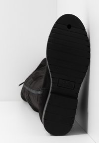 Bottine en daim noir avec une semelle en caoutchouc texturée. Détail zippé sur le côté, profil plat, et étiquette de taille visible sur la semelle.