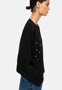 Czarny sweter dzianinowy z teksturowanym ściągaczem, ozdobiony rozrzuconymi metalicznymi cekinami. Luźny krój, okrągły dekolt i długie rękawy.