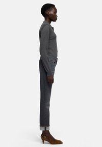 Szary sweter, jeansy z podwiniętymi nogawkami i brązowe buty na obcasie z odkrytym piętą. Widok z boku, podkreślający dopasowany krój i sylwetkę nóg.