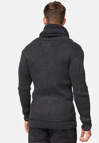 Pull en maille côtelée gris foncé avec col montant, présentant une finition texturée et des poignets et une ceinture ajustés. Vue de dos montrant un ajustement près du corps.