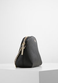 Černá látková kabelka s texturovaným povrchem, zlatým řetízkovým popruhem a zipovým uzávěrem, se zakřiveným siluetou a minimalistickým designem.