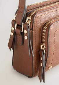 Sac en cuir texturé marron avec des zippers dorées, deux compartiments et des détails de sangle, doté de quincaillerie assortie et de coutures contrastées.