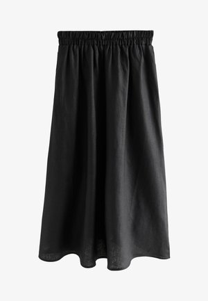 Młoda kobieta ubrana w czarną bezrękawnikową, zapinaną na guziki bluzkę i szerokie czarne spodnie stoi na drewnianym chodniku wśród dużych skał.