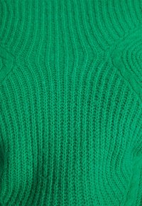 Grüner Strickstoff mit gerippter Textur und subtilen Chevron-Muster in naher Ansicht.