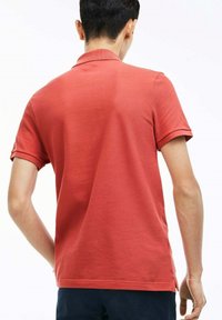 Camiseta de polo de algodón roja con un acabado texturizado, mangas cortas y cuello doblado. Aberturas laterales en el dobladillo para facilitar el movimiento.
