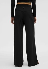 Pantalons larges noirs en tissu doux avec une taille haute sans couture. Présente un petit logo à l'arrière et une coupe fluide et décontractée.