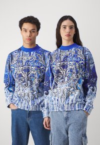 Blå mønstrede gensere har intrikate design med svulmer, blomster aksenter og teksten "CARLO COLUCCI," kombinert med denim bunner.