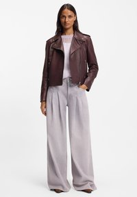 Burgundy leather jacket with asymmetrical zipper and wide lapels, paired with light gray wide-leg jeans featuring front pleats.