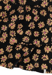 Zwarte stof met geel-oranje madeliefachtige bloemen met roze centra, die vouwen vertoont en een klein wit etiket met zwarte tekst.