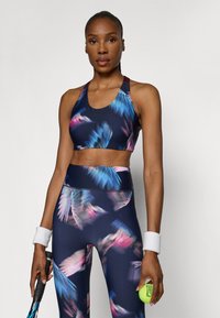 Sports-bh og leggings sett med en marineblå bunn og et fargerikt fjærmønster i blått og rosa. Laget av tøylig, atletisk stoff.