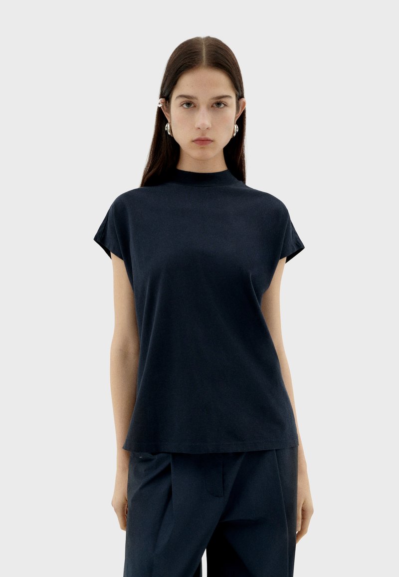 Hochgeschlossenes Top in Navyblau aus weichem Stoff mit kurzen Ärmeln und lässiger Passform, das durch minimale Nähte und eine glatte Textur besticht.