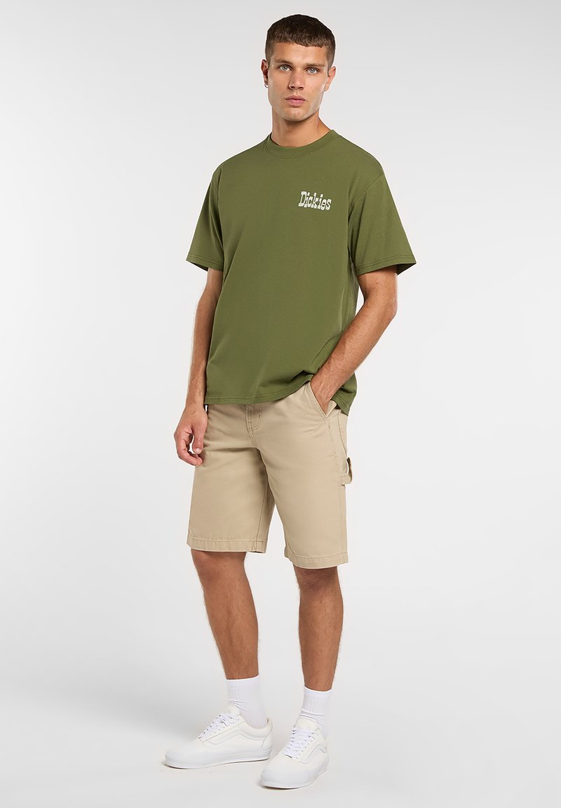 T-shirt en coton vert olive avec un col rond et des manches courtes, associé à un short cargo beige et des baskets blanches. Design simple, sans motifs.