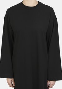 Svart oversized långärmad t-shirt med rund halsringning, tillverkad av ett mjukt bomullstyg; har sänkt axelsöm och en avslappnad passform.