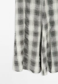 Tessuto intrecciato grigio e bianco con un motivo a griglia, caratterizzato da una texture irregolare e un design morbido, adatto per abbigliamento dalla vestibilità ampia.