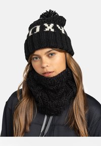 Bonnet en tricot noir avec des lettres blanches et un pompon en haut, associé à un épais col en tricot noir à encolure ronde avec un motif en relief.