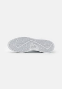 Suola di sneaker bianca con un motivo a spina di pesce. Presenta un logo visibile, una superficie liscia e bordi arrotondati per stabilità e grip.