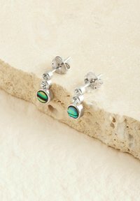 Silberne Ohrstecker mit drei klaren Edelsteinen über einem runden, schillernden Einlegestein, mit einer polierten Metalloberfläche.