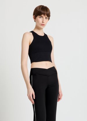 Schwarzes Crop-Top mit gerippter Textur und rundem Ausschnitt, kombiniert mit hoch taillierten schwarzen Hosen mit weißem Seitenstreifen.