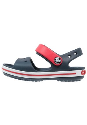 Marineblå og rød sandal med åben tå, justerbar rem, perforeret overdel, hvid sål med rød stribe og en cirkulær logo på siden.