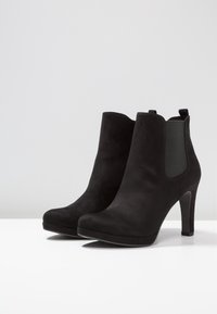Czarne zamszowe botki za kostkę na wysokim obcasie, z elastycznymi bocznymi panelami i pętelkami. Gładka tekstura i zaokrąglony kształt nosa.