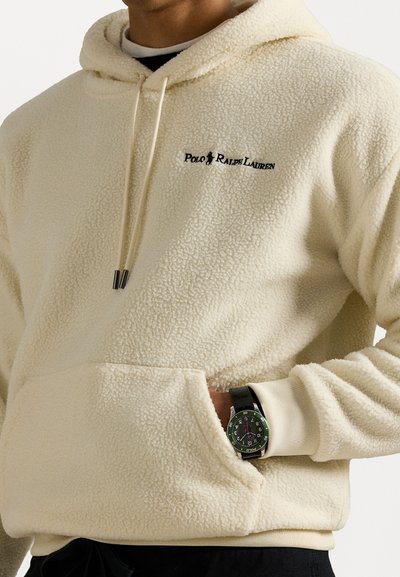 Krēms krāsas flīsa kapuce ar priekšējo kabatu, saistāmo kapuci un izšūtu "Polo Ralph Lauren" logotipu. Iezīmē ribinātas piedurknes un siltu tekstūru.