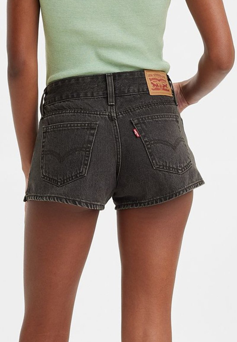 Shorts de mezclilla negra con dobladillo deshilachado, que cuentan con dos bolsillos traseros y una etiqueta de cuero con marca en la cintura. Aspecto texturizado con acabado descolorido.