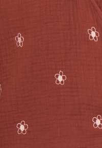Rostfarbener Stoff mit einer strukturierten Oberfläche und kleinen, gestickten weißen Blumen mit einer rosa Mitte, gleichmäßig über das Material verteilt.