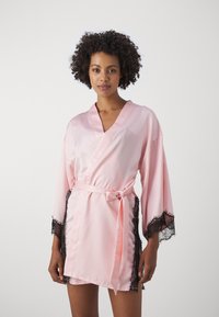 Rosa satengkåpe med lange ermer og svart blonder, omslagdesign og knytebelte i midjen. Glatt tekstur og kort lengde.